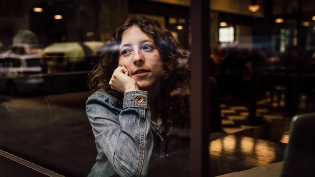 Woman sitting alone in an empty restaurant, looking out the window, symbolizing the waiting period for residency processing.